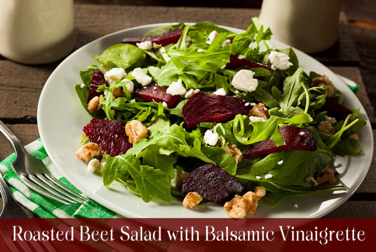 White plate with roasted beet slices, chopped walnuts and feta cheese on a bed of greens